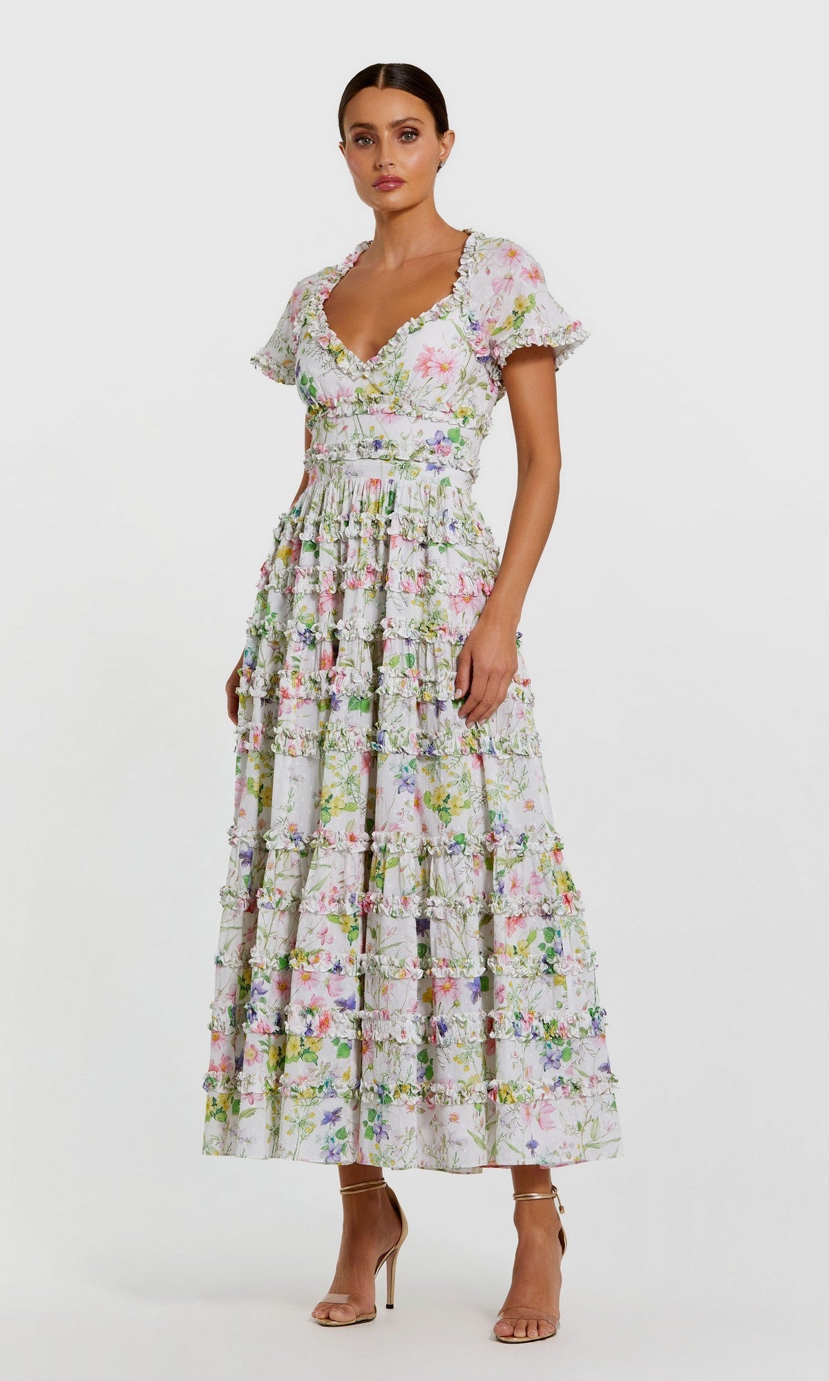 A woman stands against a plain background wearing the white multi Midi Wedding Guest Dress: Mac Duggal 8079, featuring a fit-and-flare silhouette, short sleeves, ankle-length ruffles, and nude high-heeled sandals.